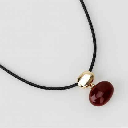 Collar con dije de piedra roja y cuenta dorada en cordón negro