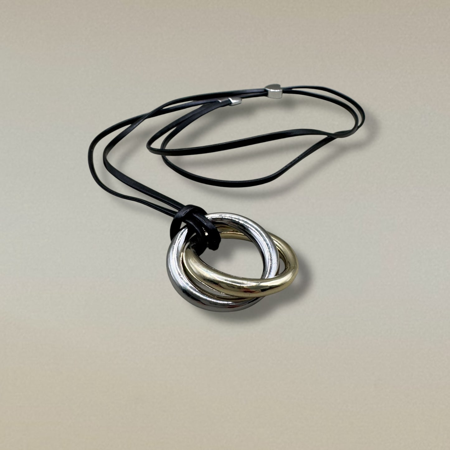Collar con aros entrelazados en dorado y plateado sobre cordón negro.