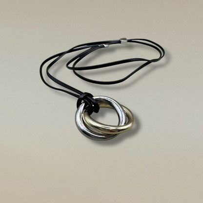 Collar con aros entrelazados en dorado y plateado sobre cordón negro.
